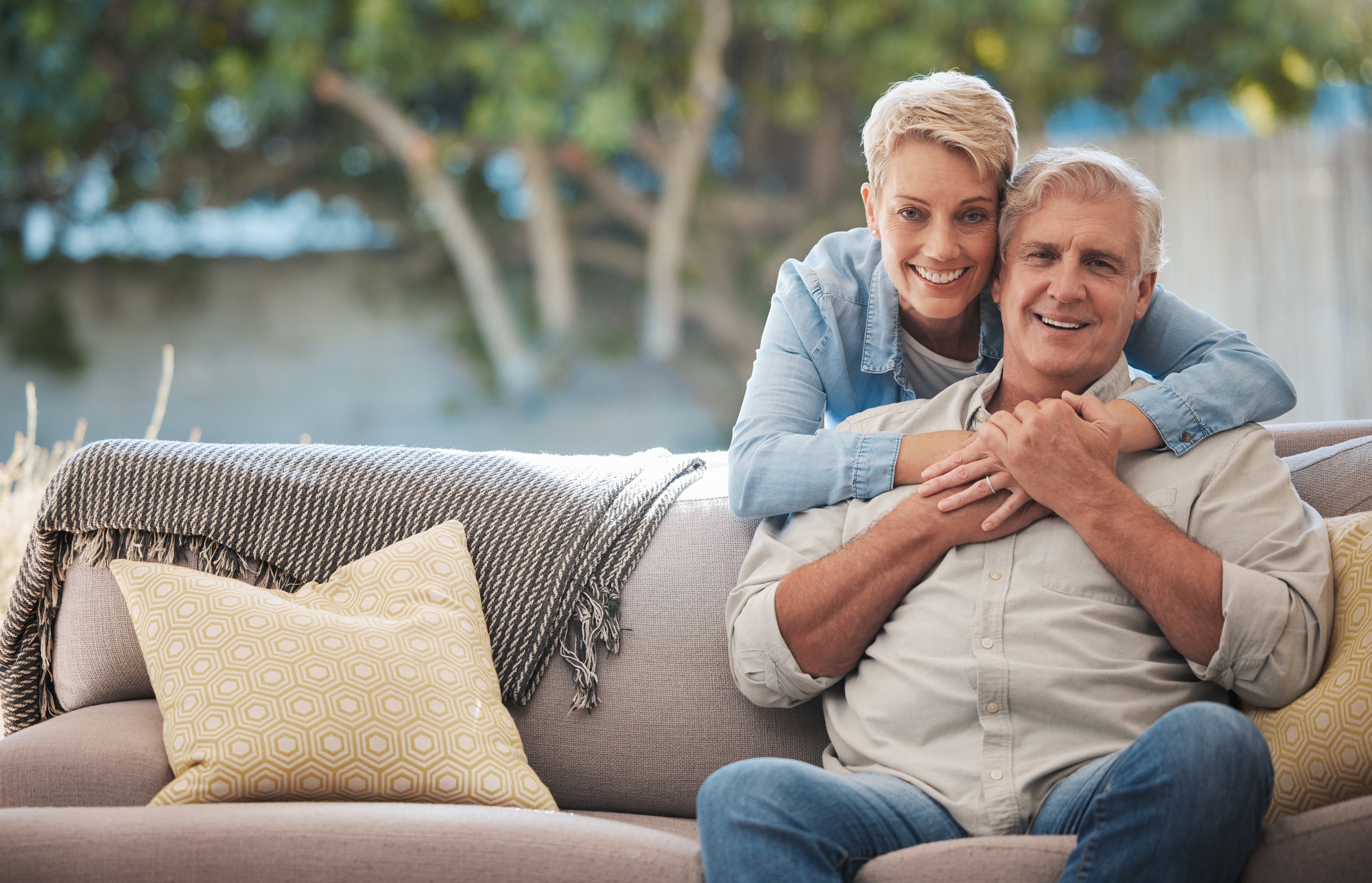 Mature couple, love bond and hug on house patio, home garden sofa and relax furniture chair in back